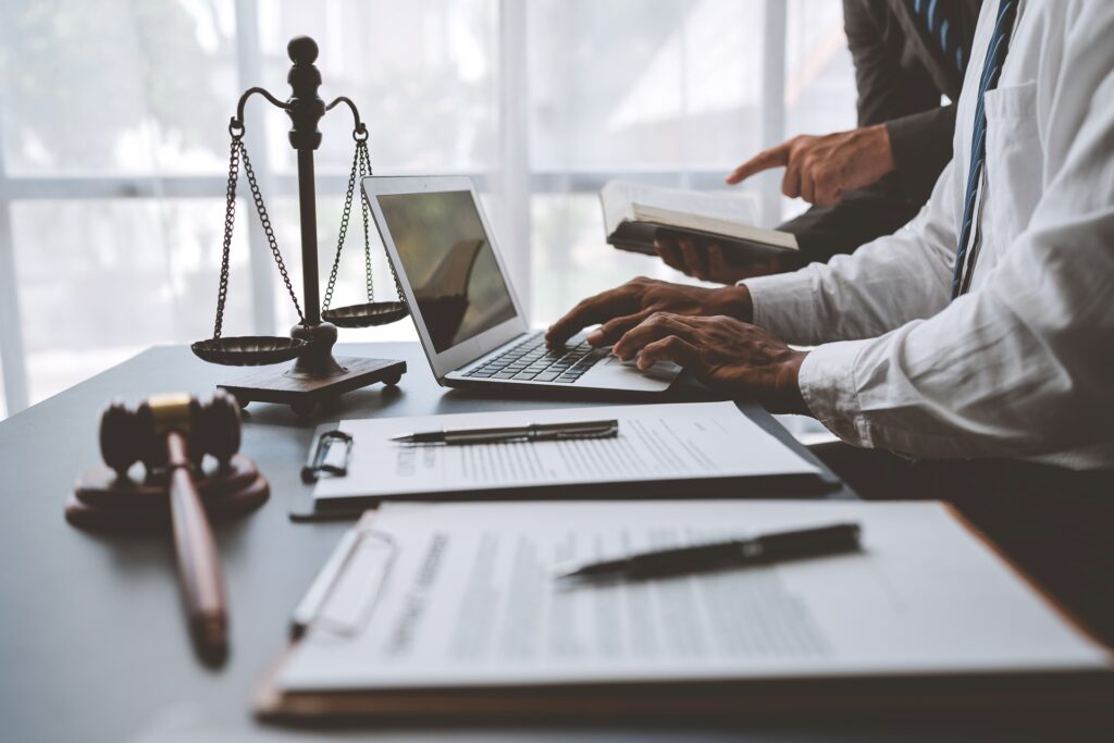 Two attorneys stand behind a desk in front of paperwork and a laptop.