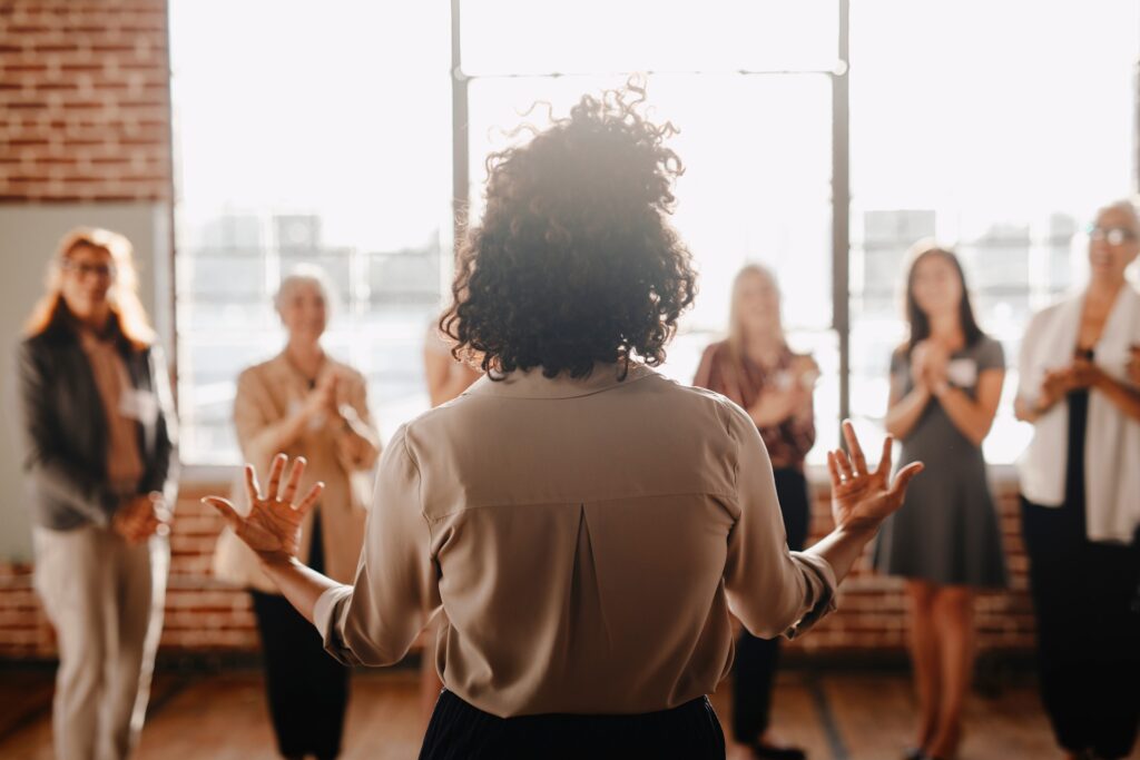 A woman stands in front of a group of employees talking expressively with her hands.